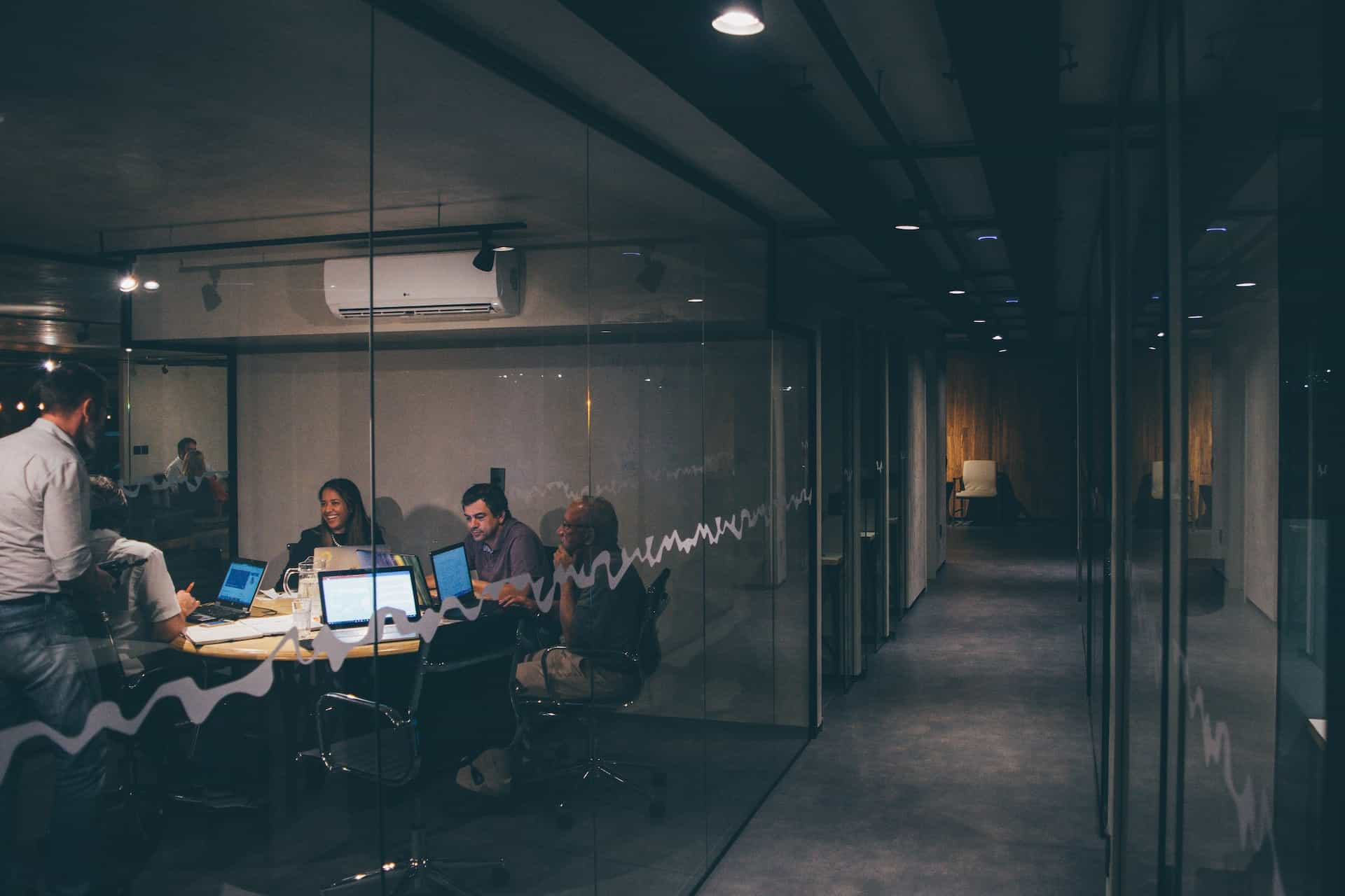 People sit around a table talking and laughing with open laptops during a work meeting.