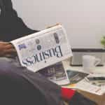 A man in a suit sitting with his legs crossed with a financial newspaper draped over one leg.