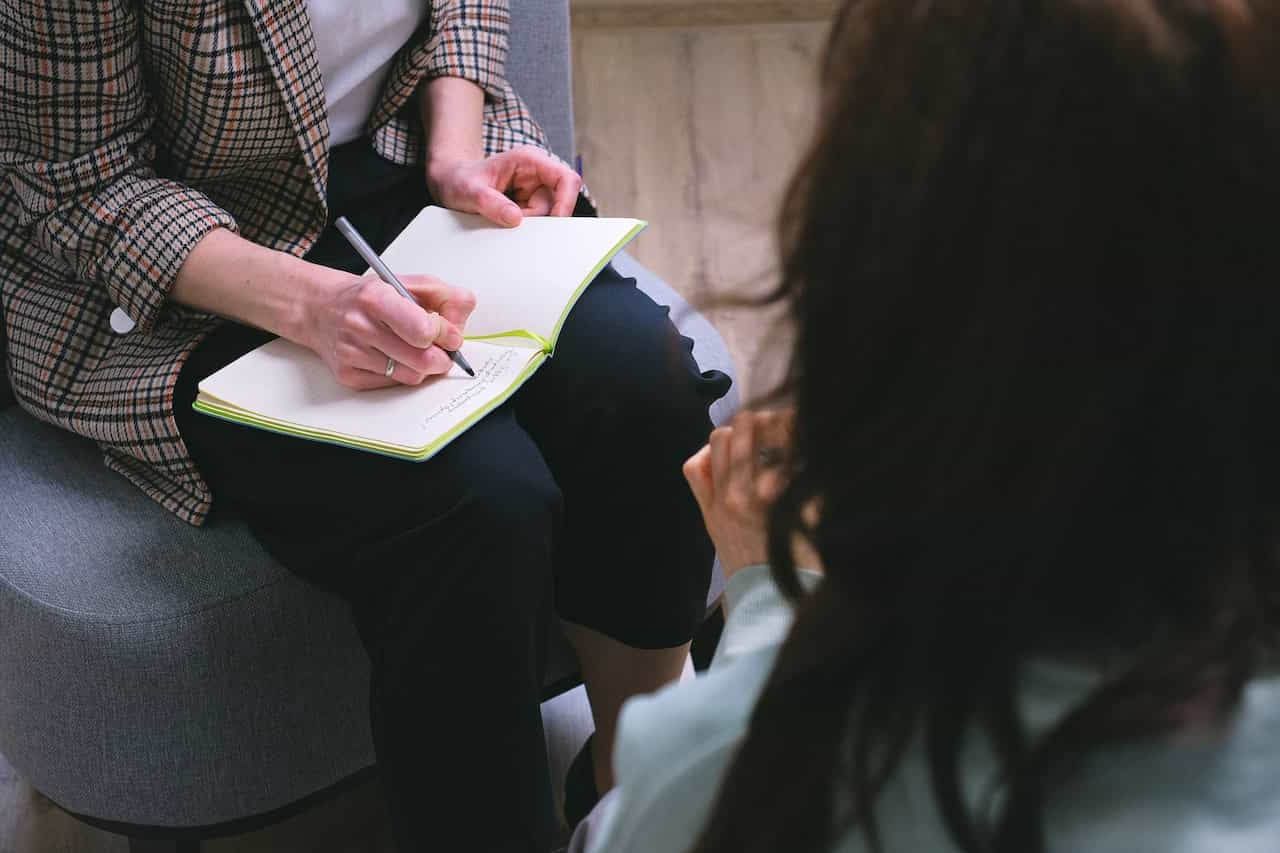 A counsellor writing in a notebook and speaking to a patient.