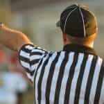 A referee in a striped uniform holds on his arm to signal to players.