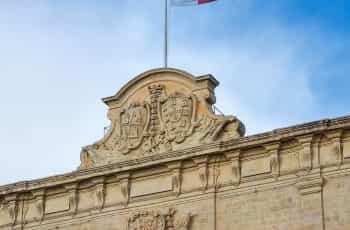 A white and red flag hoisted on a building against a blue sky.